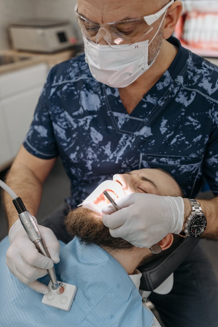 Dentist in protective gear performing dental procedure on patient in clinic.